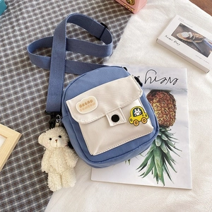 Detailed shot of a blue canvas crossbody bag with a cartoon badge and plush bear charm