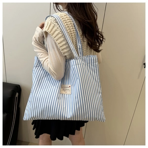 Detail of blue and white striped canvas tote bag with decorative patch on female model