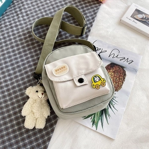 Detail of green canvas crossbody bag with cute teddy bear pendant and cartoon patches