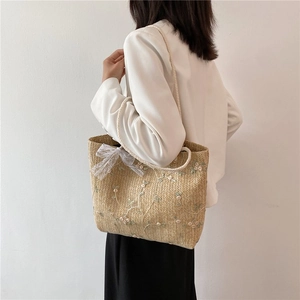 Détail d'un sac cabas en paille tissé avec broderies florales et nœud en dentelle décoratif