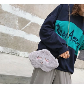 Detail of grey plush cloud crossbody bag featuring closed-eye embroidery and gold chain strap