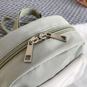 Close-up of dual metal zippers and durable twill nylon texture on light green mini bag