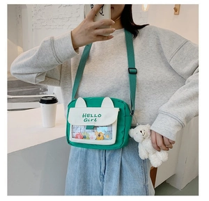 Detail of green canvas crossbody bag with cute ears, PVC window and plush bear charm