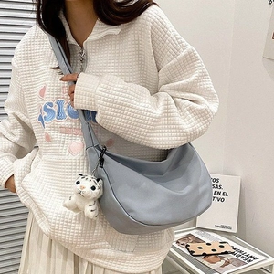 Gray-blue nylon crescent crossbody bag with cute tiger plush charm on a casual model