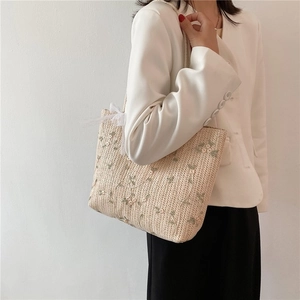 Détail du sac cabas en paille beige avec broderie florale verte et nœud en dentelle blanche