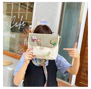 Gros plan d'un sac messager en toile crème et vert avec des badges de dessins animés mignons