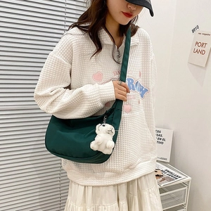 Minimalist dark green nylon crescent bag with plush tiger charm worn with casual outfit