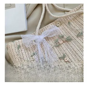 Détail d'un sac en paille tissée avec broderies florales, nœud en dentelle et fermoir métal