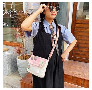 Mannequin portant un sac bandoulière en toile rose et blanc avec écussons mignons au café