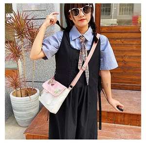Détail du sac bandoulière en toile avec rabat rose, badges cartoon et pendentifs