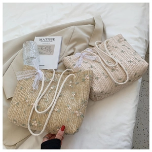 Détail de la broderie florale et du nœud en dentelle sur un sac cabas en paille