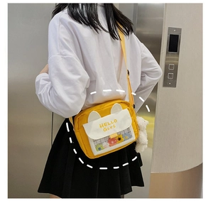 Detail of yellow cat-ear crossbody bag featuring a clear window and plush bear charm