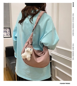 Pink nylon crescent crossbody bag with white tiger plush keychain shown on model