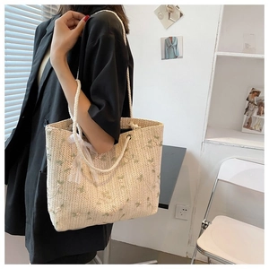 Détail du sac cabas en paille crème avec broderie florale et nœud en dentelle blanche