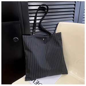 Detail of black pleated tote bag showing vertical textures and gold magnetic closure
