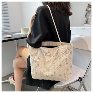 Détail de la broderie florale sur un sac en paille beige avec un nœud en dentelle blanche