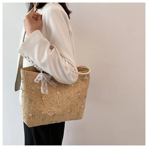 Détail d'un sac cabas en paille beige avec broderie florale rose et nœud en dentelle blanche