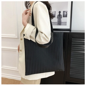 Detail of black pleated tote bag showing vertical textures and sleek shoulder strap fit