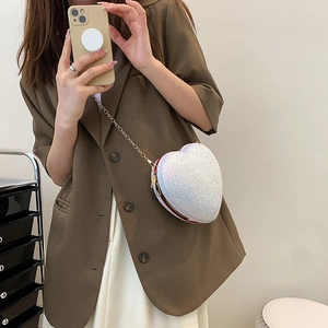 Sparkly white heart-shaped crossbody bag with gold chain strap worn by a model
