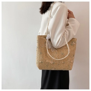 Détail du sac cabas en paille avec broderies florales et nœud en tulle sur la poignée