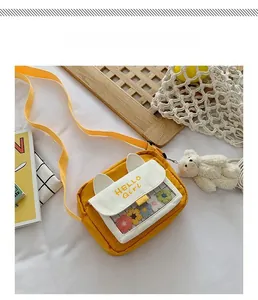 Close-up of yellow crossbody bag with cat ear flap and plush bear pendant detail