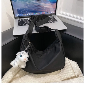 Detail of black nylon hobo bag on sofa with cute white tiger plush pendant and strap