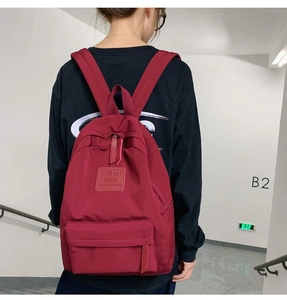 Close-up of burgundy nylon backpack with leather logo tag and hidden zipper pocket detail
