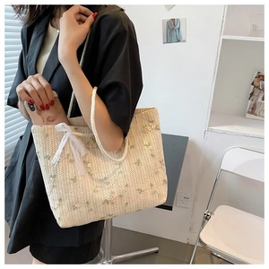 Détail de la broderie florale et du nœud en dentelle sur ce sac cabas tissé beige