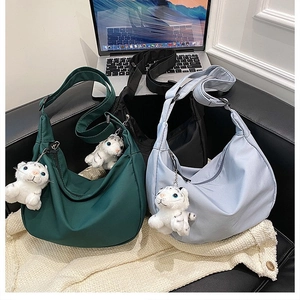 Three minimalist nylon crescent bags in green, black, and blue with tiger plush charms