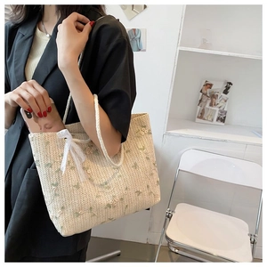 Gros plan détaillé des broderies florales et du nœud en dentelle blanche sur le sac en paille