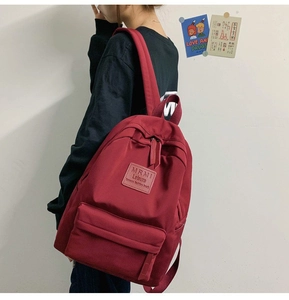 Detailed view of burgundy backpack with zipper pocket and brand label on fabric