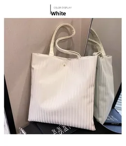 Detail view of white pleated tote bag with golden button closure and textured leather