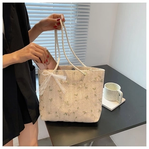 Détail d'un sac en paille beige avec broderie florale verte et nœud en dentelle blanche