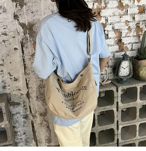 Detail of khaki canvas hobo bag showing adjustable strap and printed black text logo