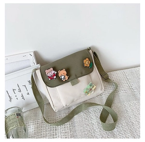 Détail du sac messager en toile avec rabat vert olive et badges de dessins animés mignons