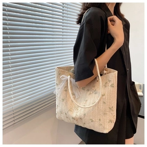 Détail du sac cabas en paille avec broderies florales et nœud en dentelle blanche