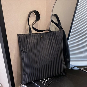 Minimalist black pleated tote bag with golden button and glossy synthetic leather texture