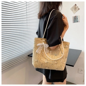 Détail du sac en paille avec broderie florale et nœud en dentelle blanche élégant