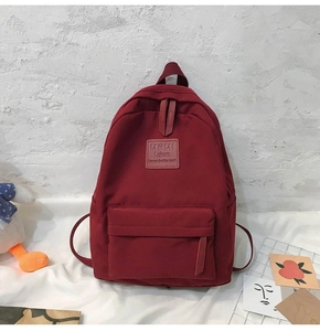Detail of burgundy nylon backpack with front zipper pocket and leisure brand label