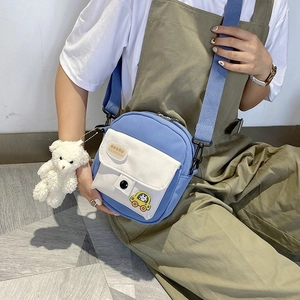 Detailed shot of a blue nylon mini crossbody bag with a plush bear charm and cartoon car patch