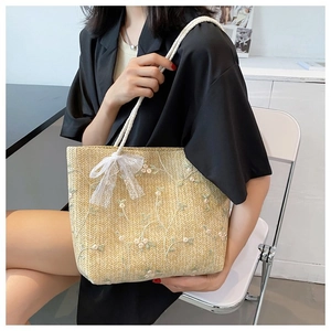 Détail du sac cabas en paille avec broderie florale blanche et un nœud en dentelle