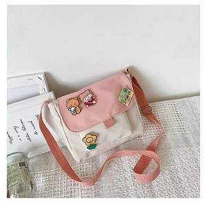 Détail du sac bandoulière en toile rose et crème avec des épinglettes de dessin animé
