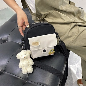 Close-up of a mini nylon crossbody bag with cute badges and a plush bear charm on a model