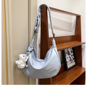 Detail of light blue crescent nylon bag with a cute white plush bear charm accessory