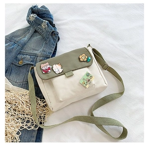 Détail du sac bandoulière en toile avec rabat vert olive et badges de dessin animé