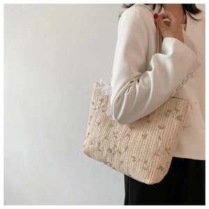 Détail du sac cabas en paille avec broderie florale verte et nœud en tulle blanc décoratif