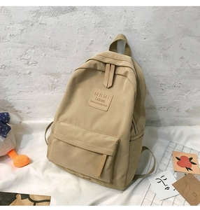 Detailed close-up of the square leather logo and premium fabric texture of the beige backpack