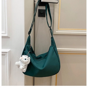 Detail of dark green crescent nylon crossbody bag with cute white tiger plush pendant