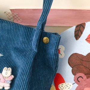 Détail d'un sac en velours côtelé bleu avec bouton doré et broche lapin mignon