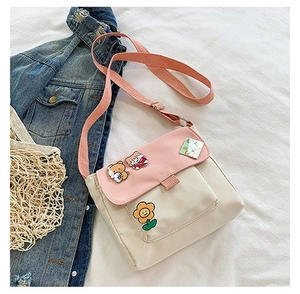 Détail du sac bandoulière en toile rose et beige avec badge ours sur lin blanc